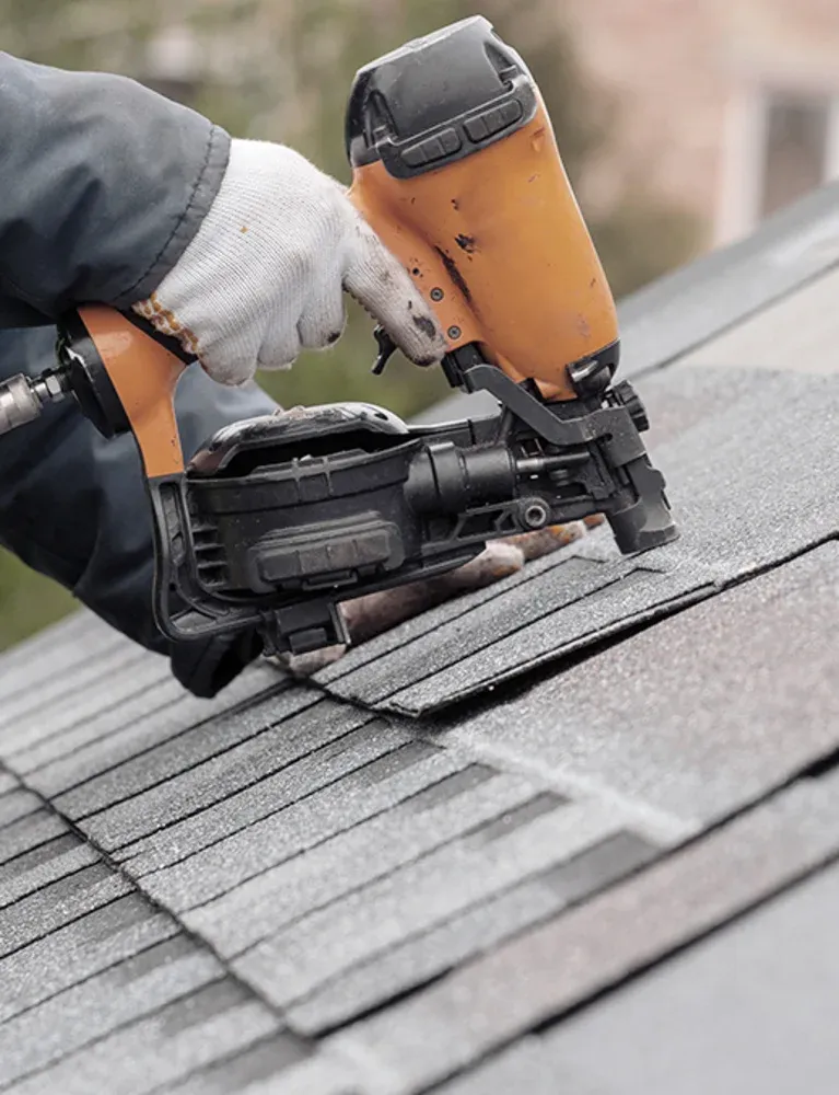 Home A worker uses a nail gun to install shingles on a sloped roof