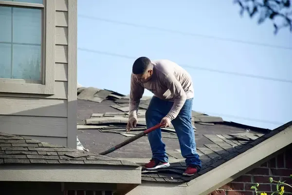 A person on a roof using a large tool to work on shingle repairs