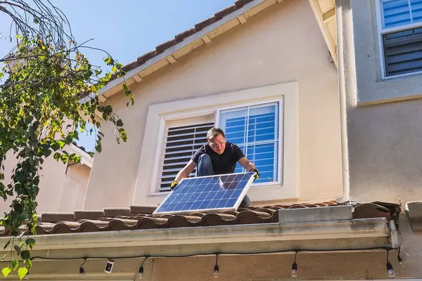 Person installing solar panel on roof. Clear blue sky