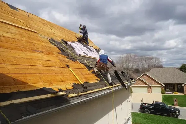 Two roofers work on a steep roof removing old shingles