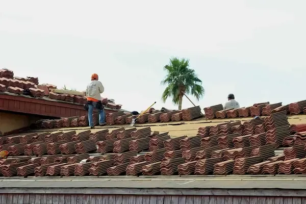 Two workers on a sloped roof are installing terracotta shingles