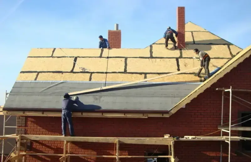 Knowlton Four workers are installing roofing material on a house under clear blue skies