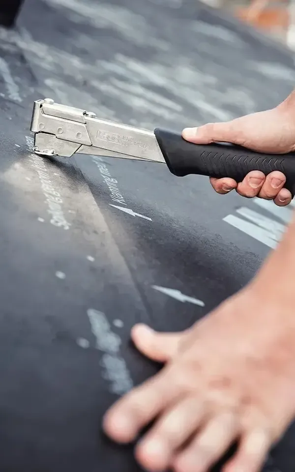 Hand using a staple gun on a black surface