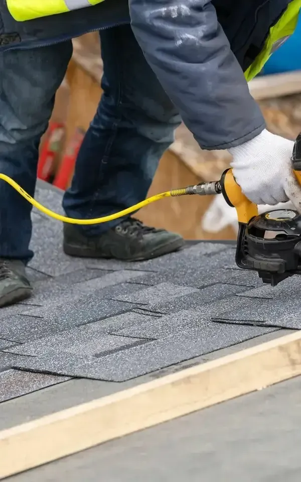 Person applying roofing shingles with a nail gun