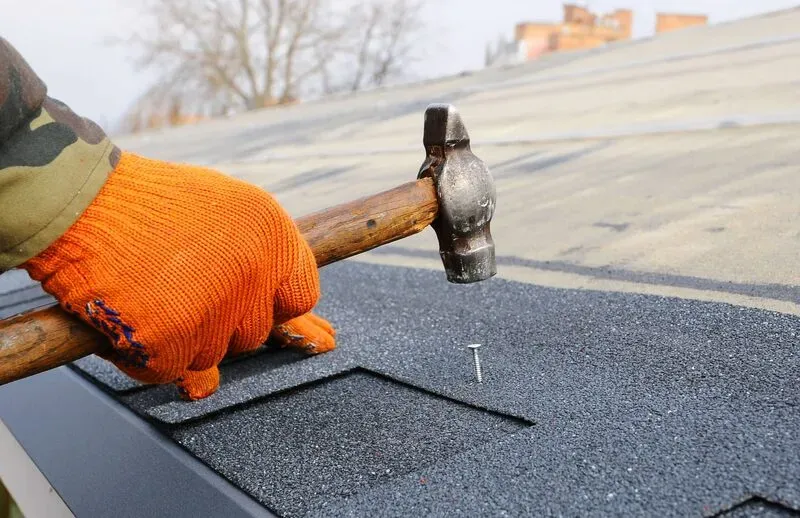 Person hammering a nail into a roof