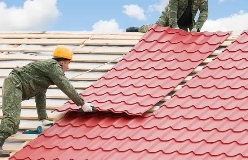Two workers installing red roof tiles