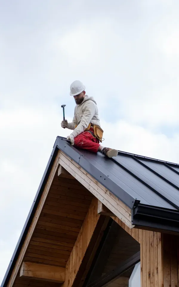 Worker on roof installing metal sheets, holding hammer